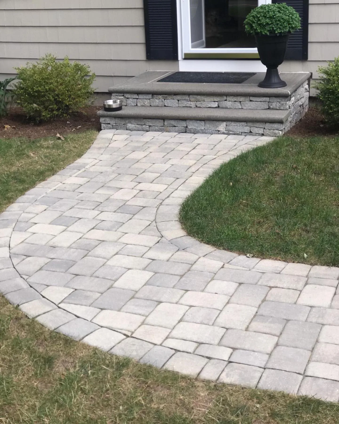 A newly installed paver walkway and steps featuring gray stone masonry and a curved path leading to a residential front door.